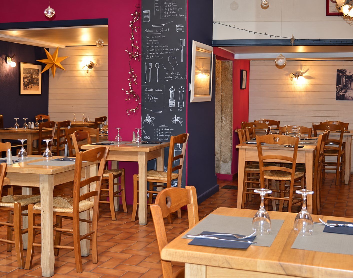 Intérieur d’un restaurant avec tables et chaises en bois, murs colorés, étoile décorative et grande ardoise couverte de dessins à la craie.